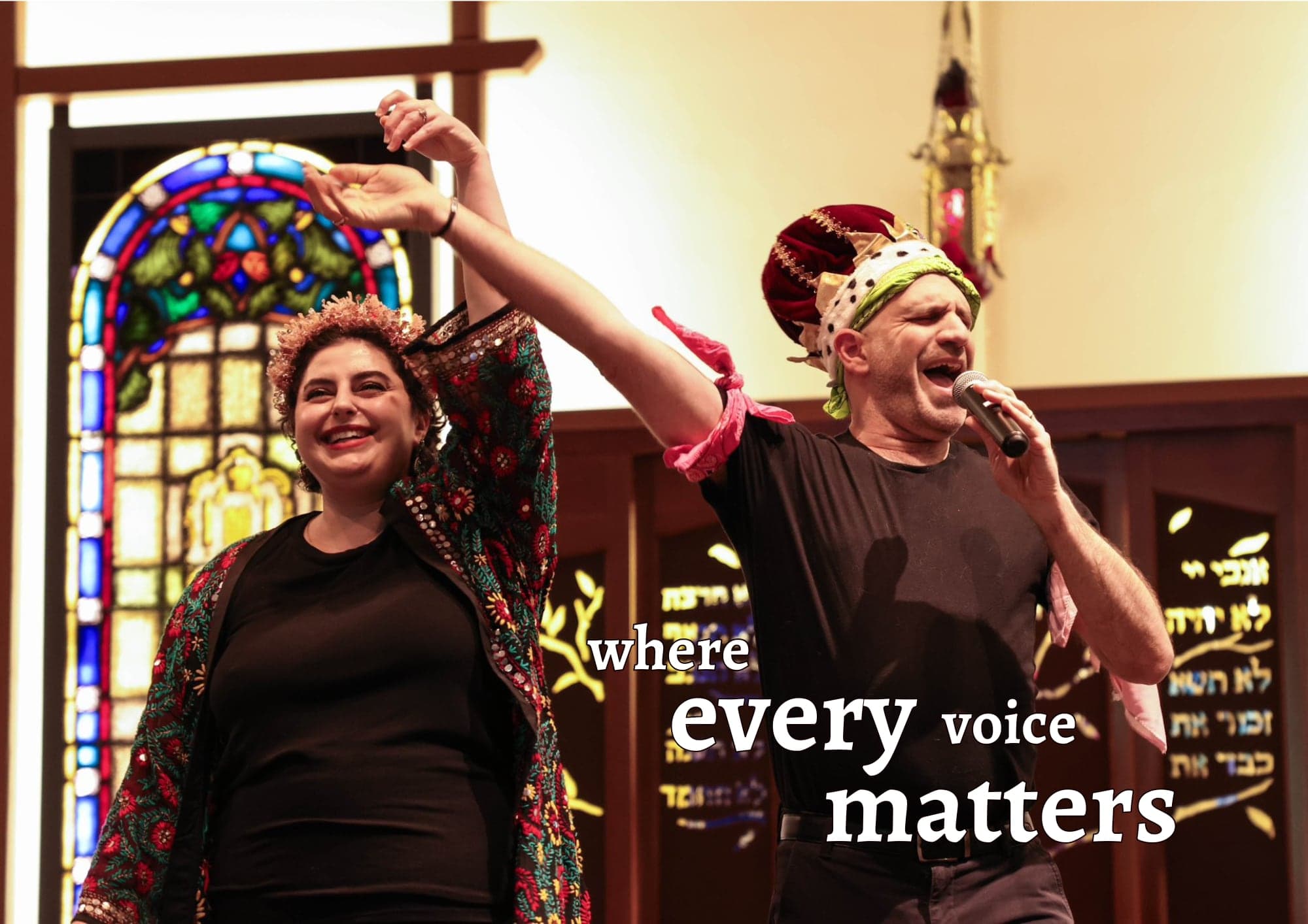 Two people in festive costumes singing and dancing in front of a stained-glass window, with the words “where every voice matters”