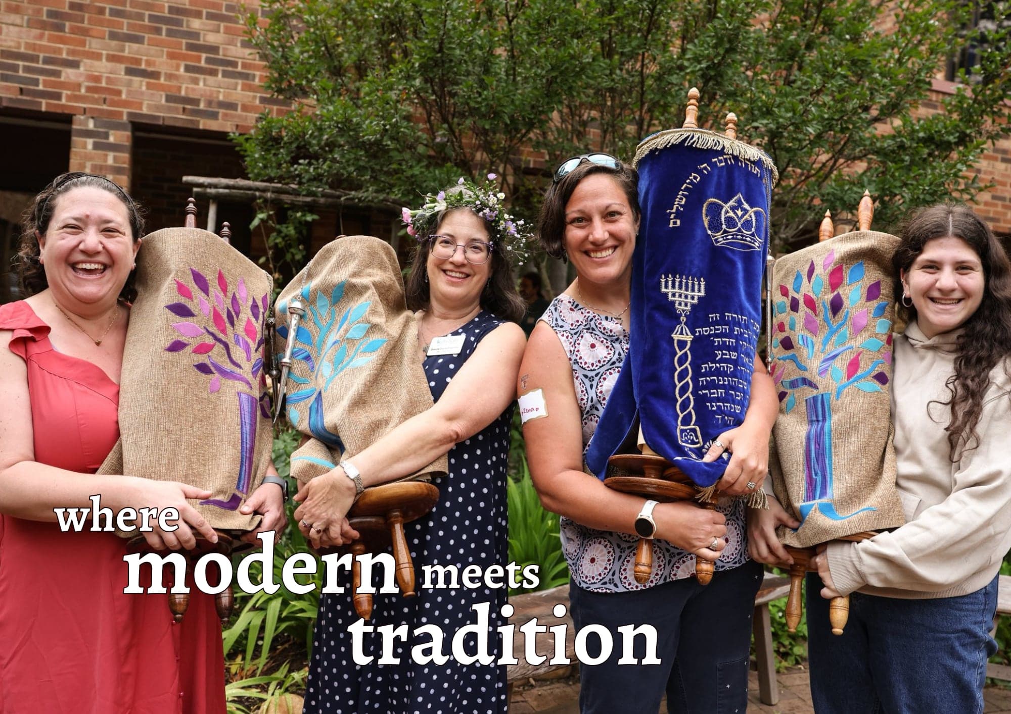 Four smiling congregants holding Torah scrolls in hand-painted covers, with the words “where modern meets tradition”